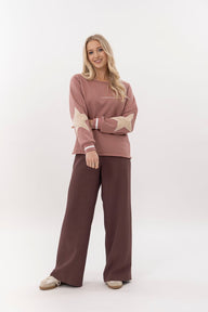 Woman wearing a pink sweater with star patterns and brown pants on a white background