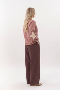 Person wearing a pink sweater with star design and brown pants on a white background