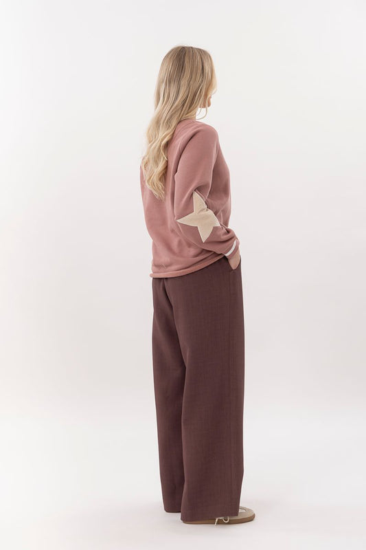 Person wearing a pink sweater with star design and brown pants on a white background