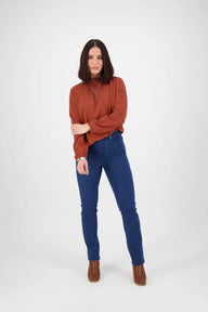 Woman wearing a rust-colored sweater and blue jeans on a white background
