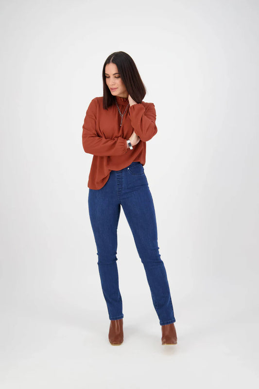 Woman wearing a rust-colored blouse and blue jeans on a white background