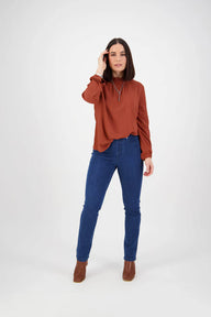 Woman wearing a rust-colored sweater and blue jeans on a white background