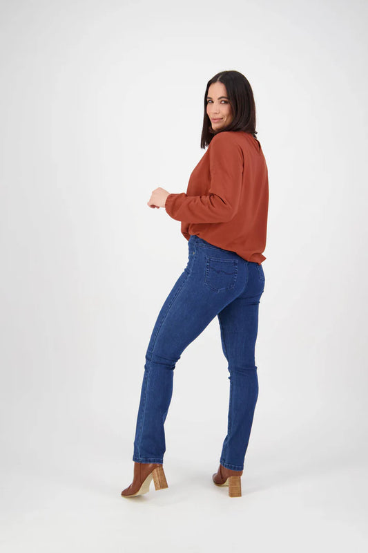 Woman wearing a rust-colored top and blue jeans on a white background