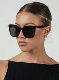 Woman wearing tort sunglasses with a plain background