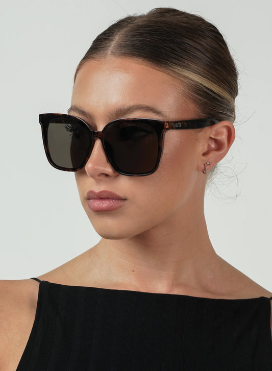 Woman wearing tort sunglasses with a plain background