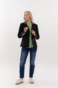 Woman wearing a black jacket with green patterned accents and blue jeans on a white background