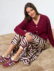 Woman wearing a maroon cardigan and zebra-patterned pants sitting on a beige surface.