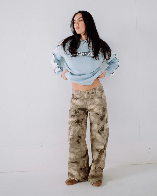 Woman wearing a light blue cropped sweatshirt and camouflage pants on a white background