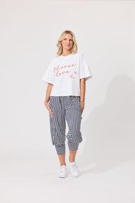 A woman wearing a white cropped t-shirt with 'Choose love x' written in red script, paired with black and white vertically striped pants, against a light gray studio background.