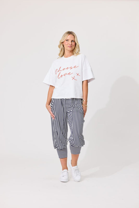 A woman wearing a white cropped t-shirt with 'Choose love x' written in red script, paired with black and white vertically striped pants, against a light gray studio background.