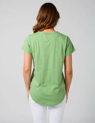 Woman wearing a green t-shirt and white pants on a plain background