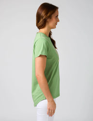 Woman wearing a green t-shirt and white pants against a plain background