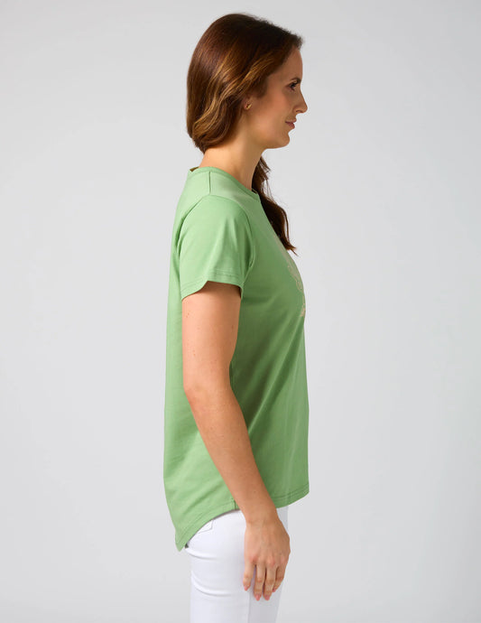 Woman wearing a green t-shirt and white pants against a plain background