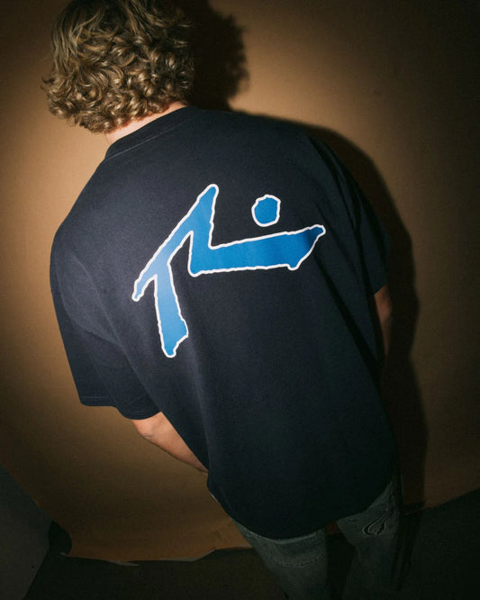Person wearing a black t-shirt with a blue graphic on the back against a brown background