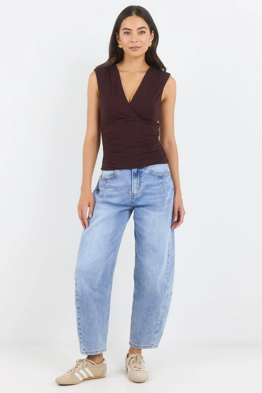 Woman wearing a brown sleeveless top and light blue jeans on a white background