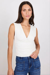 Woman wearing a white sleeveless top and blue jeans on a plain background