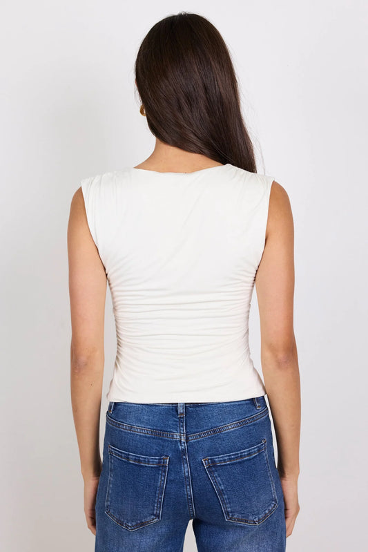 A woman viewed from the back wearing a fitted sleeveless white top and blue jeans against a plain light gray studio background.