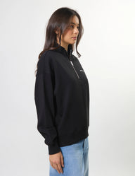 Person wearing a black zip-up sweatshirt with a small white logo on a plain background