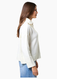 Woman wearing a white turtleneck sweater and blue jeans on a white background