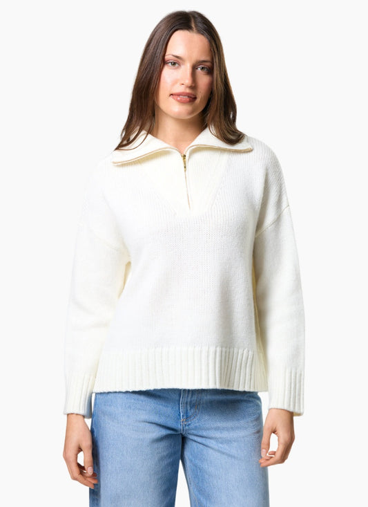 Woman wearing a white sweater with a gold zipper and blue jeans on a white background