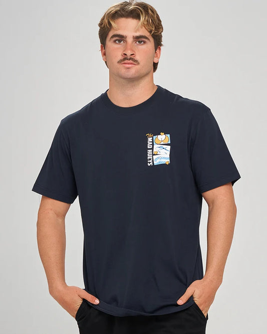 A man wearing a dark navy blue short-sleeve t-shirt with a small graphic on the left chest, posed against a light gray studio background.