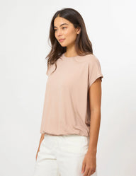A woman wearing a short-sleeve crewneck top in a dusty rose pink color, paired with white pants, photographed against a clean white studio background.