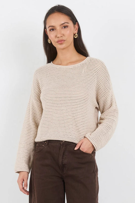 Woman wearing a beige knitted sweater and brown pants against a white background