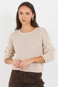 Woman wearing a beige knitted sweater and brown pants on a white background