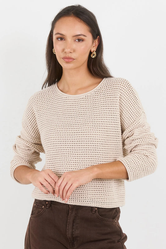 Woman wearing a beige knitted sweater and brown pants on a white background