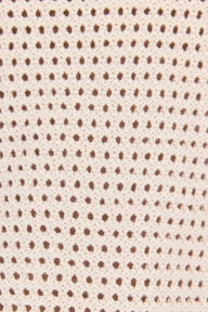 Close-up of a knit fabric texture featuring a repeating pattern of small brown dots on a warm cream or beige background.