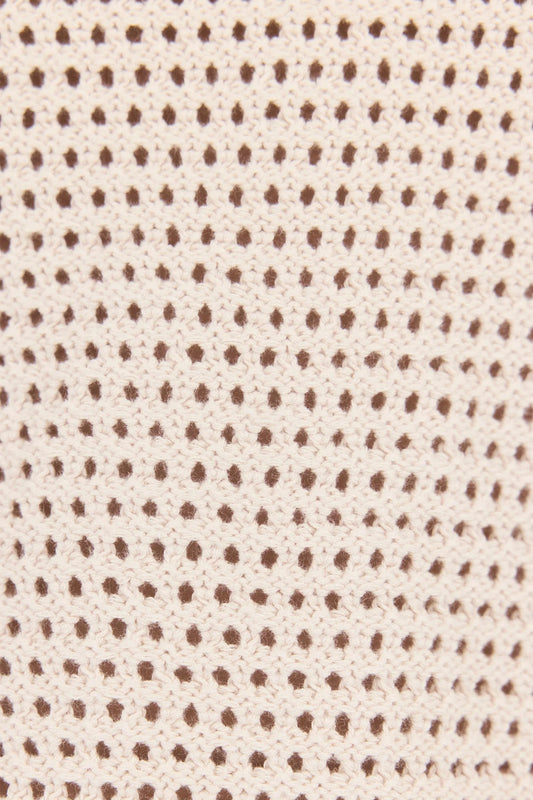 Close-up of a knit fabric texture featuring a repeating pattern of small brown dots on a warm cream or beige background.