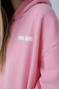 Pink hoodie with 'GOOD GOODS' text on a plain background