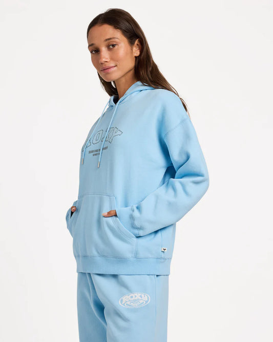 Person wearing a light blue hoodie and pants with branding on a white background