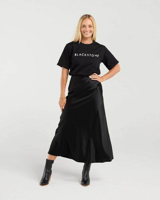 Woman wearing a black 'BLACKSTONE' t-shirt and black skirt on a white background