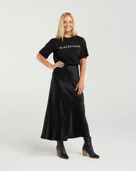 Woman wearing a black 'BLACKSTONE' t-shirt with a black skirt on a white background