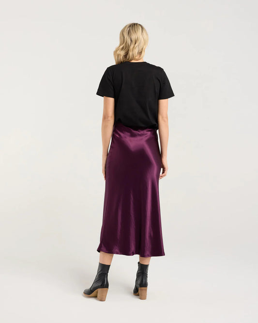 Woman wearing a black t-shirt and purple satin skirt on a white background
