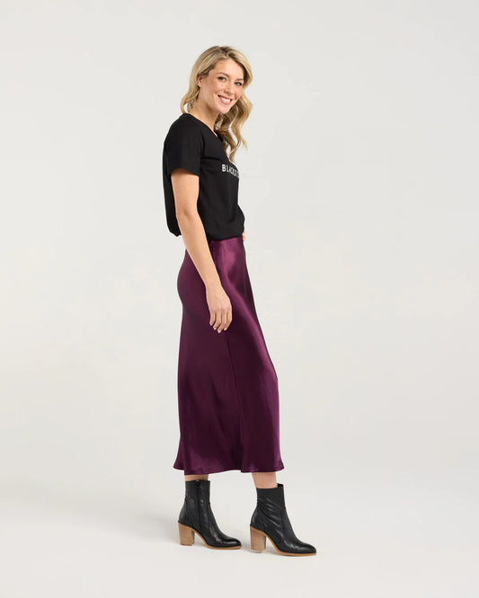 Woman wearing a black t-shirt and purple satin skirt on a white background