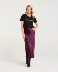 Woman wearing a black t-shirt with 'BLACKSTONE' text and a purple satin skirt on a white background
