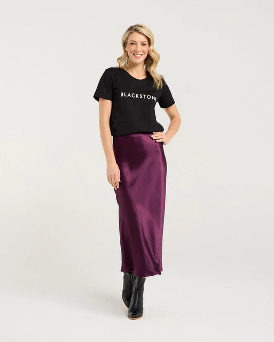 Woman wearing a black t-shirt with 'BLACKSTONE' text and a purple satin skirt on a white background