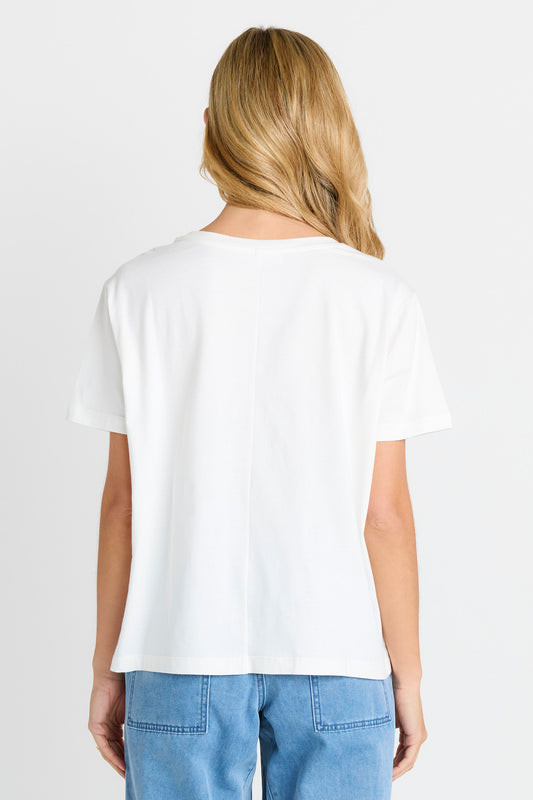 A woman viewed from the back wearing a plain white short-sleeve crewneck T-shirt and light blue jeans against a light gray studio background.