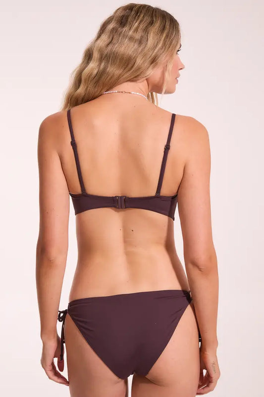 Woman wearing a dark purple bikini on a light pink background