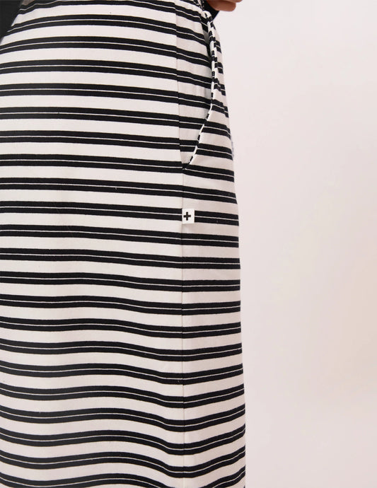 Close-up of a black and white horizontally striped garment, likely a skirt or dress, with a small white square patch featuring a black cross on the front, set against a plain off-white background.