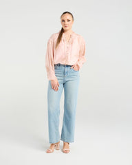 Woman wearing a light pink blouse and light blue jeans on a white background