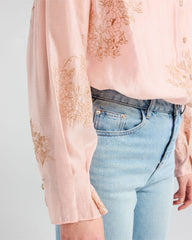 Light pink blouse with floral embroidery and light blue jeans on a plain background