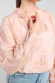 Person wearing a light pink blouse with lace details and blue jeans on a plain background