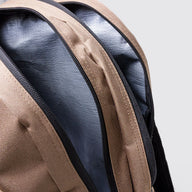 Close-up detail of a backpack showing the tan woven exterior, black zipper, and dark gray interior lining against a light gray background.