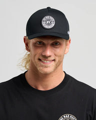 Man wearing a black cap and black shirt with a logo on a gray background