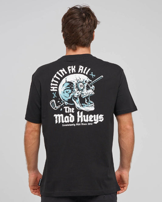 A man viewed from behind wearing a black t-shirt with a large graphic print on the back. The graphic features a white and light blue skull with a golf club, the text 'HITTIN FK ALL' arched above, and 'The Mad Hueys' below in a distressed font.