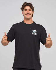 A man wearing a black crewneck t-shirt with a small white and blue graphic on the left chest, posing with both thumbs up against a solid gray background.