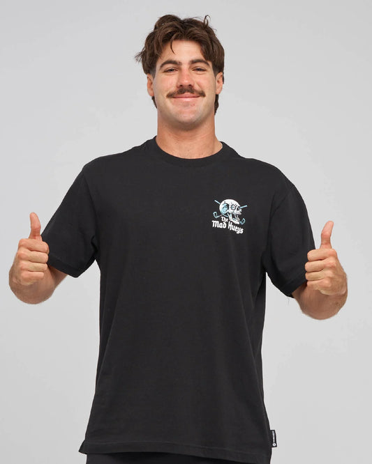 A man wearing a black crewneck t-shirt with a small white and blue graphic on the left chest, posing with both thumbs up against a solid gray background.
